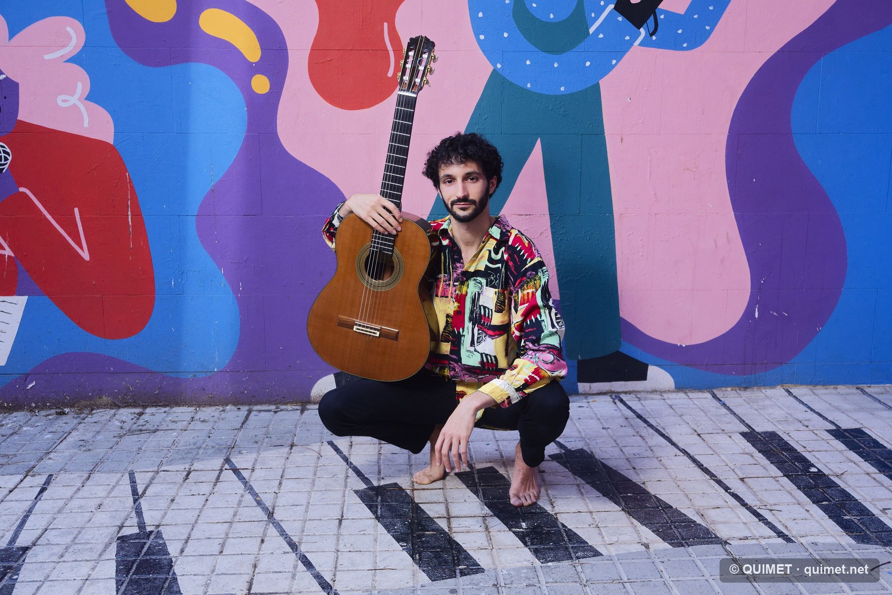 Retrat d’un guitarrista davant un mural de colors